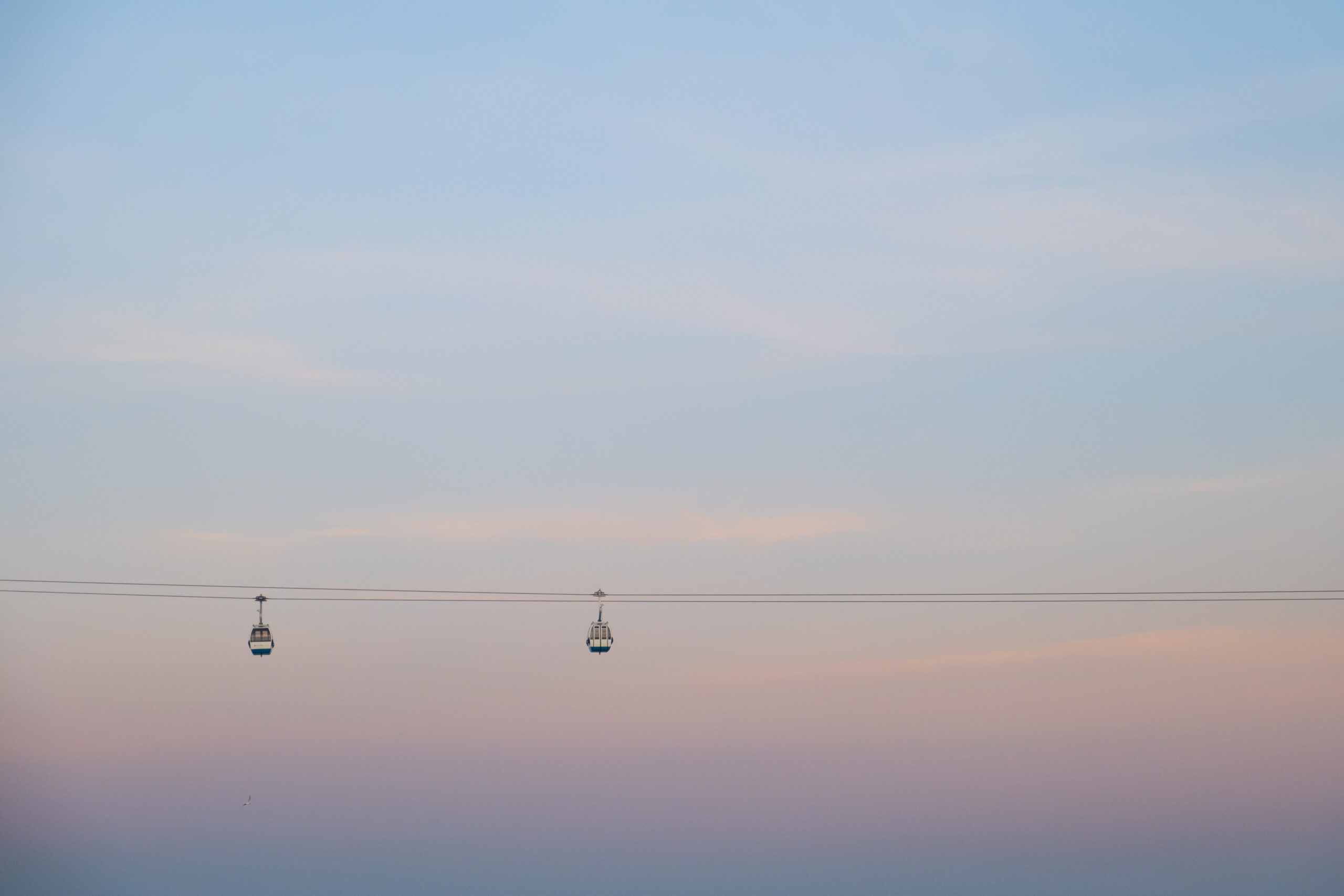 Two cable cars suspended against a blush sunset sky over Lisbon, Portugal